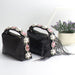 Black handbag with decorative pearls and feathers on a white surface.