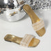 Gold sandals with rhinestone straps next to a disco ball on a reflective surface