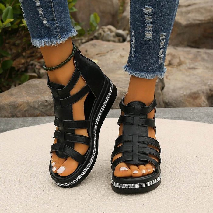 Black strappy sandals worn with ripped jeans on a neutral background
