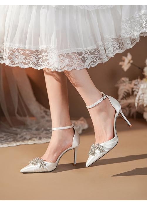 White satin high-heeled shoes with embellishments worn with a white lace dress.