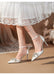 White satin high-heeled shoes with embellishments worn with a white lace dress.