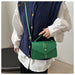A person wearing a navy cable-knit vest over a white long-sleeve blouse, carrying a green top-handle crossbody bag with gold-tone hardware.