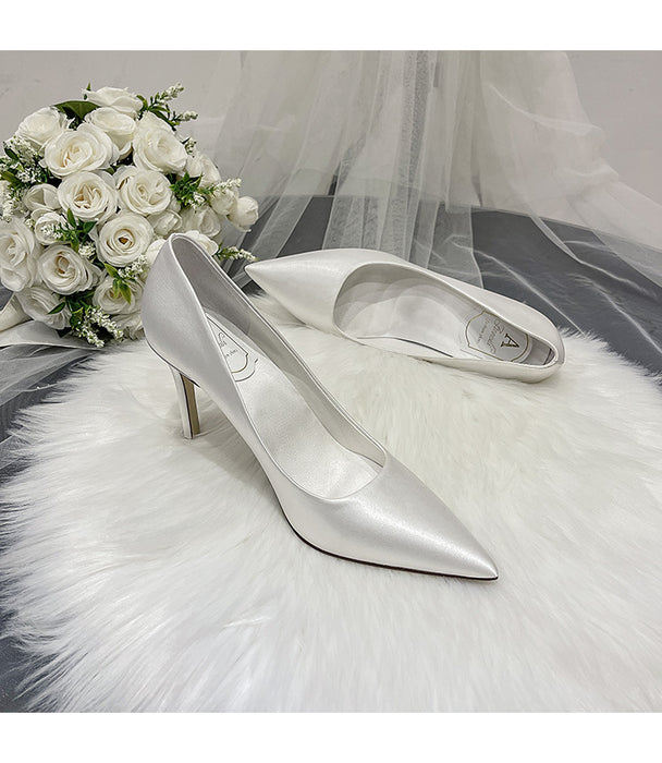 Silver high-heeled shoes on a white fur surface with a bouquet of white roses in the background.