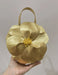 Gold flower-shaped handbag held by a hand against a plain background
