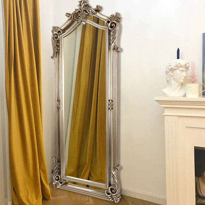 Decorative silver mirror with intricate designs in a room with yellow curtains and a fireplace.