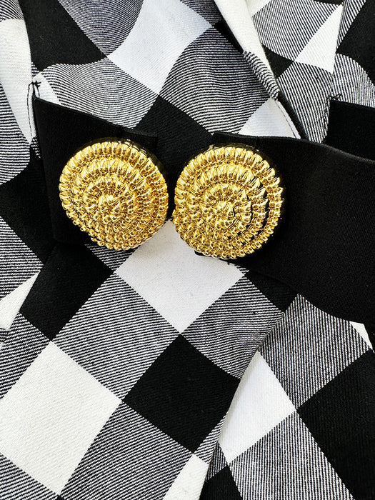 Gold circular earrings on a black and white checkered fabric background