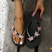 Black flip-flops with butterfly decorations worn on feet, placed on a wooden surface.