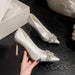 White high-heeled shoes with crystal embellishments on a dark surface, held by a hand.