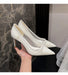 White high-heeled shoes held by a hand against a marble wall.