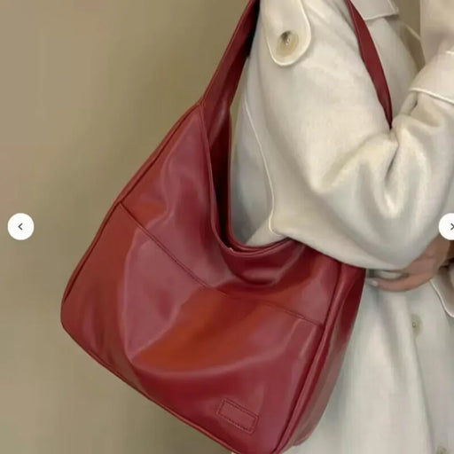 Red handbag held by a person wearing a light-colored coat against a neutral background