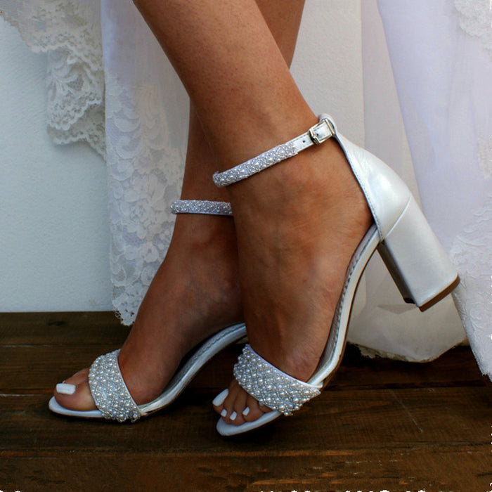 White wedding shoes with pearl embellishments on a wooden floor.