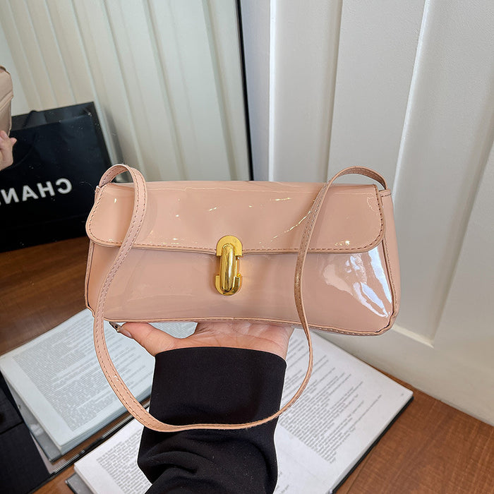 A glossy light pink patent leather shoulder bag with a gold turn-lock clasp, held by a hand over an open book in front of a white paneled door.