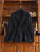 A black tailored blazer-style jacket with a wrap front and drawstring waist, hanging on a hanger in front of a wooden cabinet.
