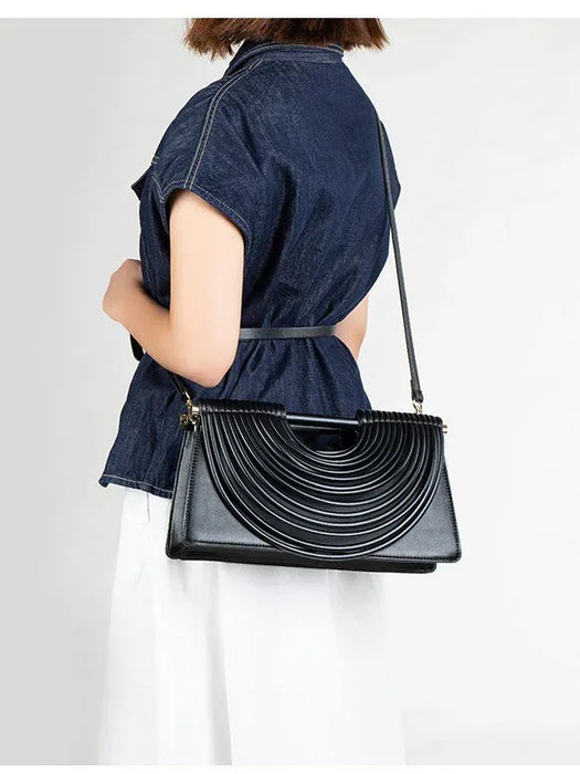 Person wearing a denim shirt holding a black handbag with a unique design on a white background