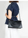 Person wearing a denim shirt holding a black handbag with a unique design on a white background