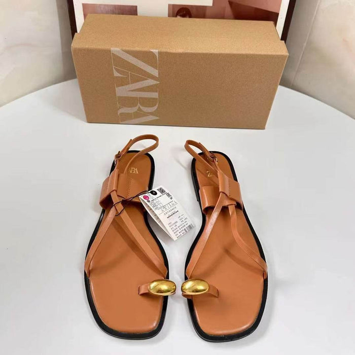 Pair of tan sandals with gold accents on a white surface, next to a Zara box.
