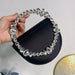 Black handbag with crystal embellishments held by a hand against a neutral background