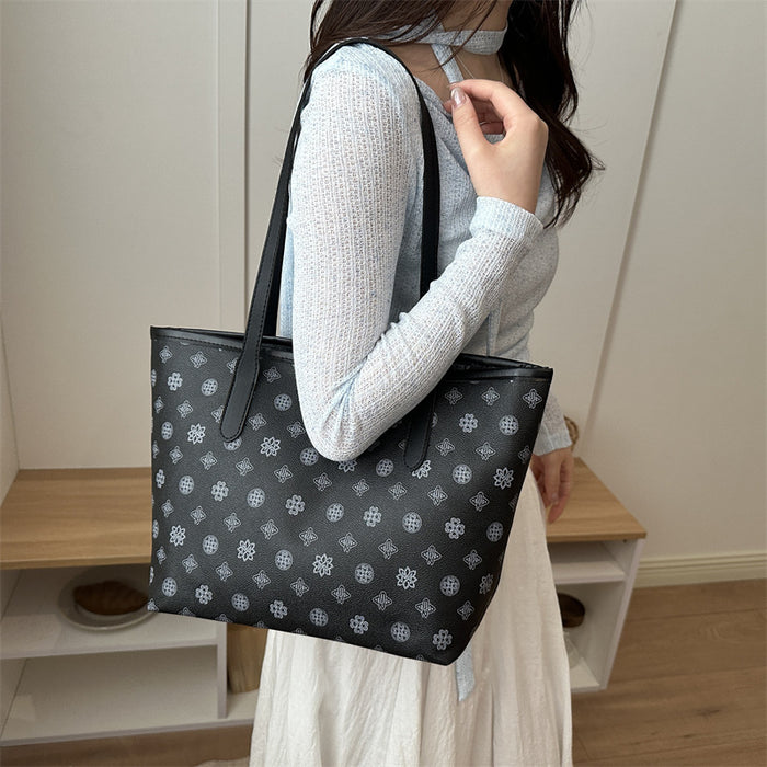 A woman wearing a light gray knit top and white skirt carries a large black tote bag with a repeating white geometric pattern and black shoulder straps in an indoor setting.