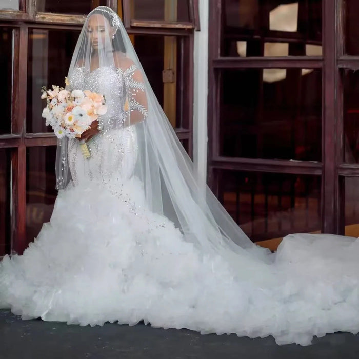 Bride in a white wedding dress with a long veil holding a bouquet indoors.