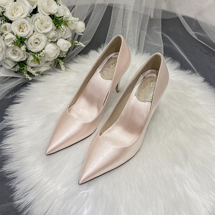 Pair of pink high-heeled shoes on a white fur surface with a bouquet of white roses.