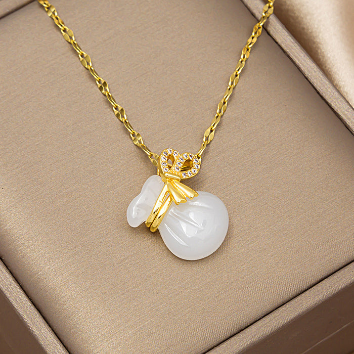 A gold chain necklace with a pendant featuring a carved white jade-like rabbit and a small gold heart-shaped charm with tiny clear stones, displayed inside a beige jewelry box.