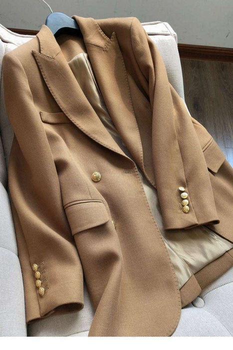 A camel brown wool blazer with gold buttons, draped over a light beige armchair.