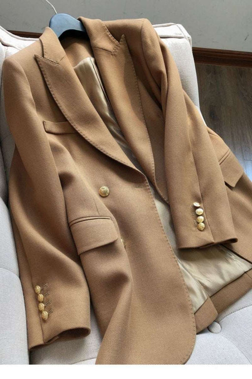 A camel brown wool blazer with gold buttons, draped over a light beige armchair.