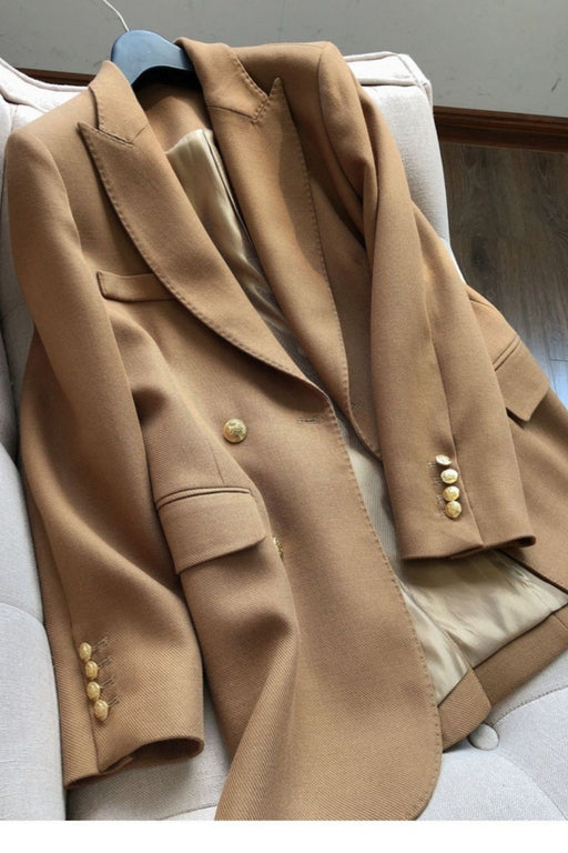 A camel brown wool blazer with gold buttons, draped over a light beige armchair.