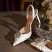 White high-heeled shoes with decorative embellishments on a reflective surface.