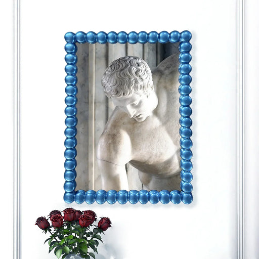 Statue in a blue beaded frame with red roses below on a white background