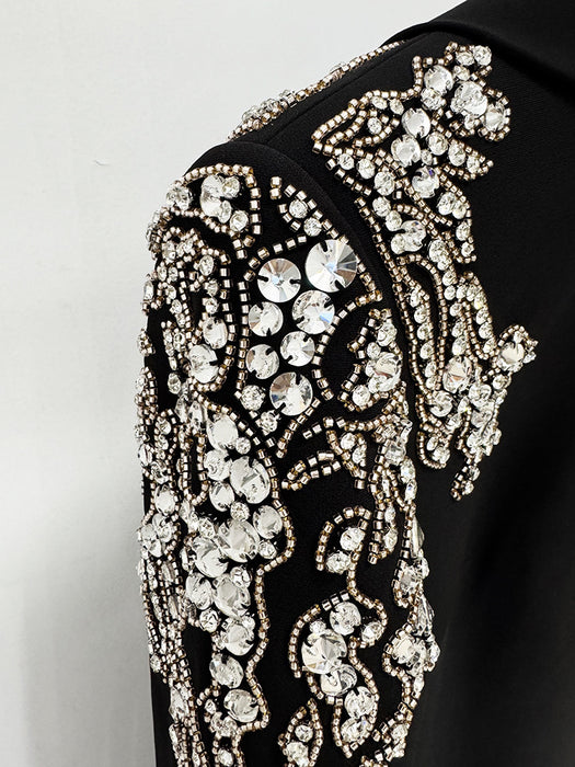 Close-up of a black garment with intricate gold and crystal embellishments on a white background