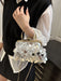A close-up of a person wearing a black sweater vest over a white blouse, holding a small structured handbag covered in reflective silver and white disc embellishments with a gold-tone frame and chain strap.