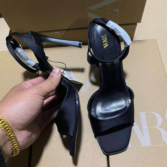 Black high-heeled sandals with 'Zara' branding on a cardboard surface.