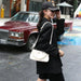 Woman in black outfit with white handbag walking on a street.