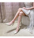 Woman wearing silver high-heeled shoes and a white lace dress against a neutral background