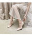 Person wearing light pink high-heeled shoes and a sheer white skirt.