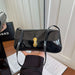 A black patent leather shoulder bag with a gold turn-lock clasp, held by a hand in front of a white paneled door. A black Chanel shopping bag is visible in the background on the left.