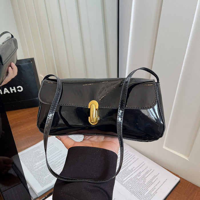 A black patent leather shoulder bag with a gold turn-lock clasp, held by a hand in front of a white paneled door. A black Chanel shopping bag is visible in the background on the left.