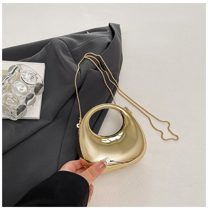 Gold handbag with chain strap held by a hand on a neutral background