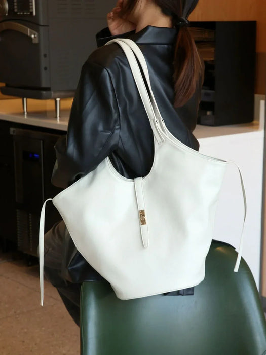 Person wearing a black leather jacket with a white handbag on a green chair.