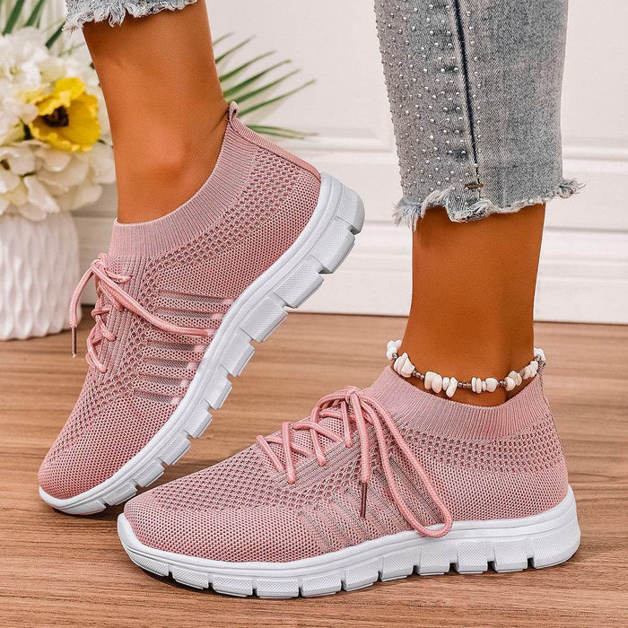 Pink sneakers with white soles worn by a person on a wooden floor.