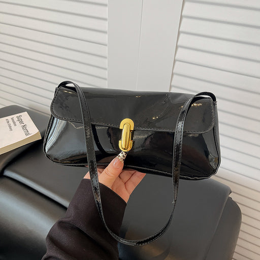 Black handbag with gold clasp held by a hand against a neutral background