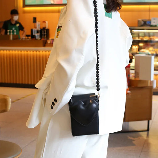 Person wearing a white coat with a black heart-shaped bag in an indoor setting