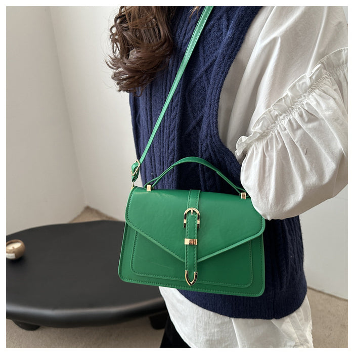 A woman wearing a navy blue cable-knit vest over a white puff-sleeve blouse carries a bright green leather shoulder bag with a top handle and gold-tone hardware.