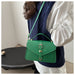 A woman wearing a navy blue cable-knit vest over a white puff-sleeve blouse carries a bright green leather shoulder bag with a top handle and gold-tone hardware.