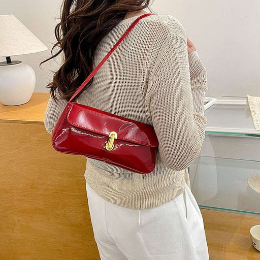 Person wearing a beige sweater and white pants with a red handbag over their shoulder in an indoor setting.