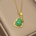 Gold pendant necklace featuring a green jade-like gourd pendant with a halo of small clear stones, displayed on a beige jewelry box.