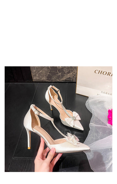 White high-heeled shoes with floral details held by a hand on a dark surface.