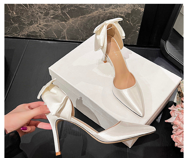 Pair of white high-heeled shoes with a bow on a black marble surface.