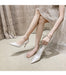 White high-heeled shoes worn by a person sitting on a beige surface with a neutral curtain background.